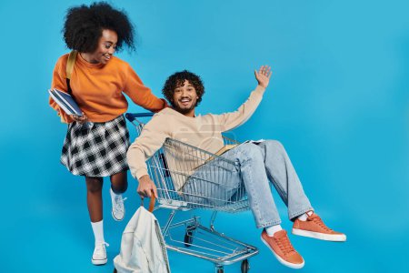 A playful couple of interracial students in casual attire, sitting together in a shopping cart, enjoying a fun moment.