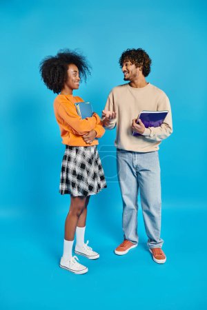An interracial couple standing united in casual attire against a vibrant blue backdrop.