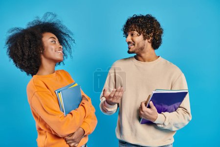 Dos estudiantes interracial se paran de cerca sobre un telón de fondo azul en un ambiente de estudio, mostrando unidad y diversidad.