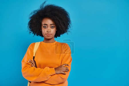 A stylish African American woman with a voluminous afro stands confidently in front of a vibrant blue background.