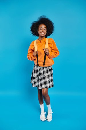 Téléchargez les photos : Une étudiante afro-américaine se tient avec confiance en tenue décontractée dans un cadre bleu vif dans un studio. - en image libre de droit