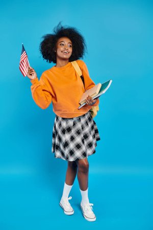 Ein afroamerikanisches College-Mädchen steht mit einem Buch in der einen und einer amerikanischen Flagge in der anderen Hand und strahlt Patriotismus aus.