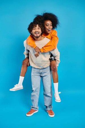 Foto de Una pareja interracial, dos estudiantes, compartiendo un abrazo sincero en un fondo de estudio azul. - Imagen libre de derechos