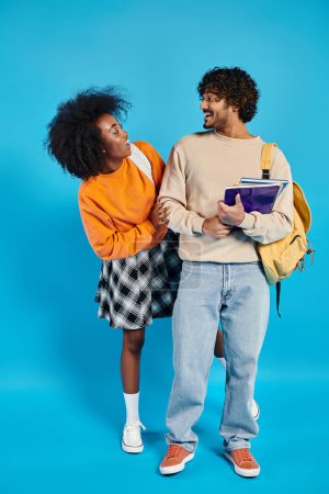 A couple of interracial students standing together in casual attire on blue backdrop in a studio setting.