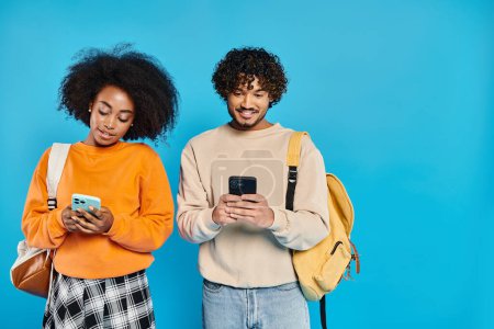 Photo for A multicultural couple of students standing side by side with smartphones in a studio, showcasing unity and friendship. - Royalty Free Image
