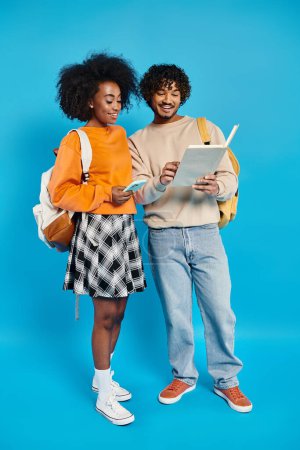 Foto de Una pareja interracial de estudiantes parados uno al lado del otro en atuendo casual sobre un fondo azul en un estudio. - Imagen libre de derechos