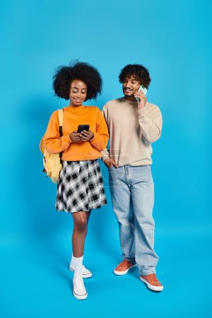 Téléchargez les photos : Couple d "étudiants interracial en tenue décontractée debout les uns à côté des autres sur fond bleu en studio. - en image libre de droit