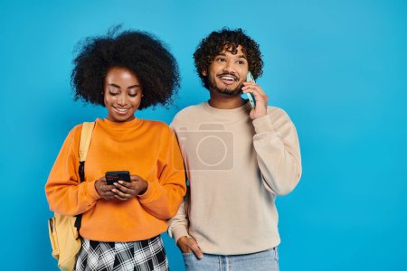 Téléchargez les photos : Un couple interracial d "étudiants réunis en tenue décontractée sur fond bleu dans un décor de studio. - en image libre de droit