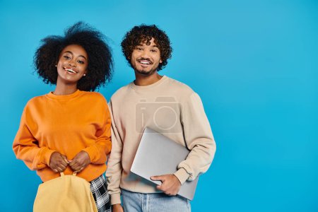 Un couple interracial d'étudiants debout ensemble en tenue décontractée sur fond bleu.