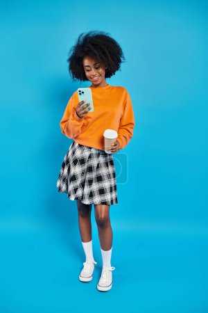 Une femme noire se tient devant un fond bleu vibrant, tenant un téléphone portable.