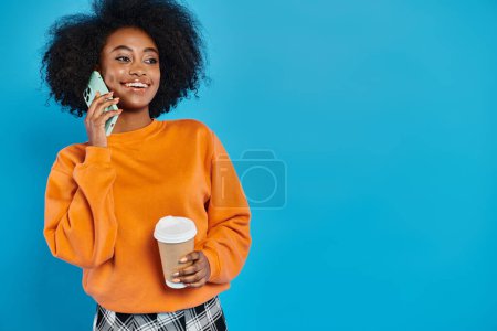 A woman of color holding a coffee cup while engaged in a phone conversation, set against a blue backdrop.
