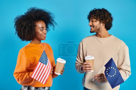 An interracial couple in casual attire standing together, holding coffee cups and flags
