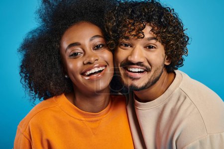 A man and woman, representing interracial harmony, smile brightly in a studio with a blue backdrop.