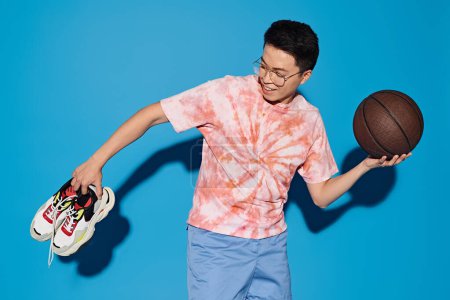A stylish young man confidently holds a basketball and shoes, exuding enthusiasm and readiness for sports.