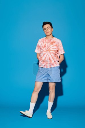 A stylish, good-looking young man in trendy attire posing actively in front of a vibrant blue backdrop.