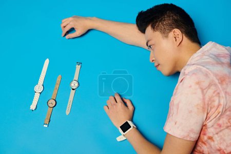 Photo for A stylish young man in trendy attire laying on the ground next to three watches, appearing contemplative. - Royalty Free Image