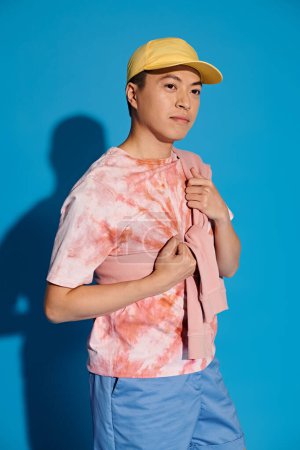 A stylish young man in a tie-dyed shirt poses actively on a blue backdrop.