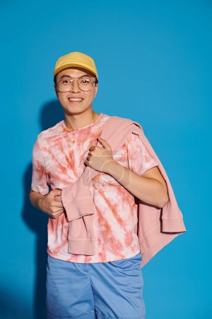 Stylish young man posing energetically in a trendy pink shirt and blue shorts against a vibrant blue backdrop.