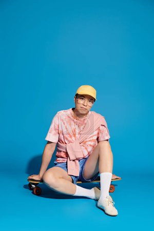 Ein stilvoller junger Mann in trendiger Kleidung sitzt mit einem Skateboard auf dem Boden und umarmt einen Moment der Entspannung.