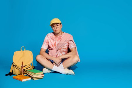Foto de Un joven con estilo se sienta en el suelo rodeado de una mochila y libros, profundamente en el pensamiento y el estudio. - Imagen libre de derechos