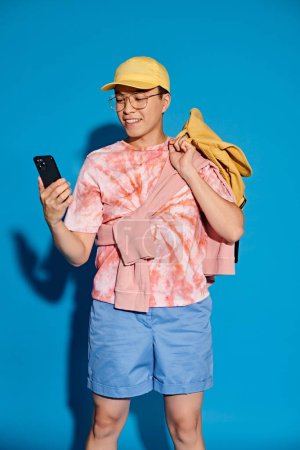 Un jeune homme élégant avec un sac à dos et un téléphone portable, respirant un sentiment d'aventure et de connectivité moderne dans un contexte bleu.