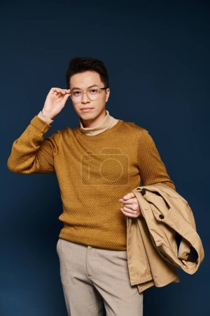 A fashionable young man poses actively in a brown sweater and tan pants, exuding elegance and style.