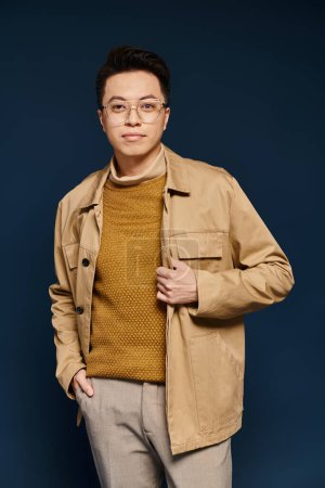 A fashionable young man confidently poses in a tan jacket and glasses, exuding elegance and charm.