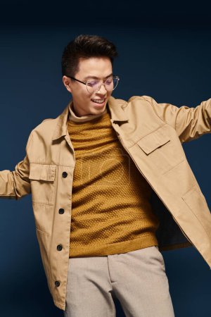 A fashionable young man in glasses and a tan jacket strikes a pose, exuding confidence and sophistication.