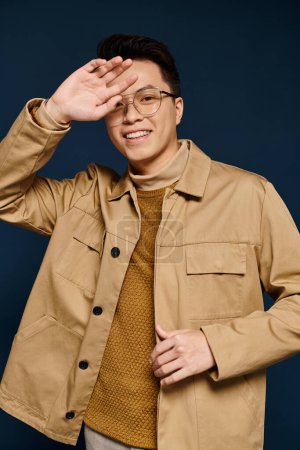 A fashionable young man with glasses poses confidently in a tan jacket, exuding elegance and sophistication.