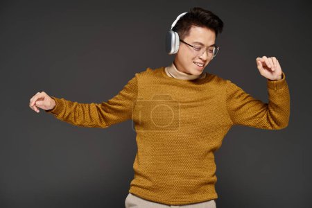 Photo for A fashionable young man in a sweater is actively posing while wearing headphones. - Royalty Free Image