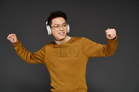 Photo for A fashionable young man energetically poses in a cozy sweater while wearing headphones, exuding a trendy and sophisticated vibe. - Royalty Free Image