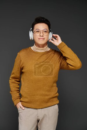 Ein modischer junger Mann im kuscheligen Pullover lauscht aufmerksam durch elegante Kopfhörer und strahlt gelassene Zuversicht aus..