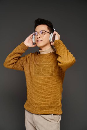 Un homme élégant dans un pull brun et des lunettes écoute de la musique à travers des écouteurs.