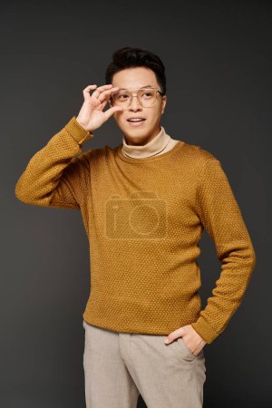 Téléchargez les photos : Un jeune homme à la mode dans un élégant pull marron frappant une pose confiante pour la caméra. - en image libre de droit