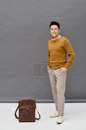 Téléchargez les photos : Un jeune homme à la mode en tenue élégante se tient à côté d'un sac brun, style exubérant et mystère. - en image libre de droit