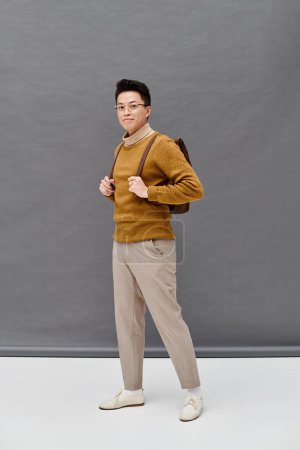 Téléchargez les photos : Un jeune homme à la mode en pull marron et pantalon blanc frappe une pose dynamique. - en image libre de droit