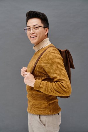 Ein stilvoller junger Mann mit Brille und braunem Pullover posiert elegant.