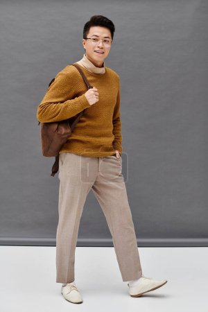 A fashionable young man strikes a dynamic pose in a brown sweater and tan pants, showcasing his elegant attire.