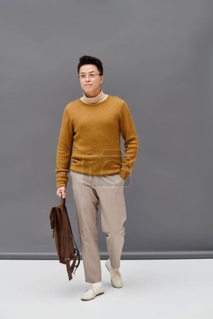 Un joven con estilo en un suéter marrón y pantalones blancos posa con confianza.