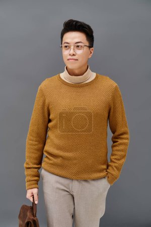 A fashionable young man in a brown sweater and tan pants strikes a dynamic pose.