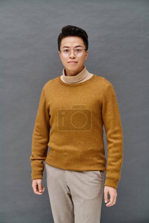 A fashionable young man in a brown sweater and tan pants poses confidently, showcasing his elegant attire.