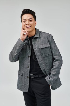 Téléchargez les photos : Un jeune homme à la mode prend une pose dynamique dans une veste grise élégante et une chemise noire, exsudant sophistication et confiance. - en image libre de droit