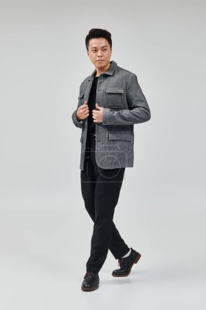 A fashionable young man in a gray jacket and black pants striking a dynamic pose.