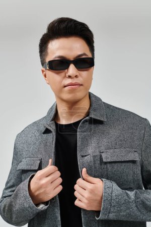 Un jeune homme à la mode posant avec confiance dans des lunettes de soleil et une veste élégante.