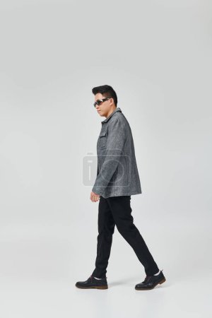 Un joven con estilo en una chaqueta gris y pantalones negros paseando con confianza.