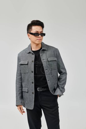 Téléchargez les photos : Un jeune homme à la mode pose avec confiance dans une veste grise et un pantalon noir. - en image libre de droit