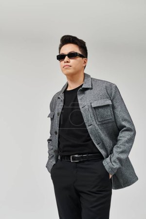 Téléchargez les photos : Un jeune homme à la mode pose activement dans une veste grise et une chemise noire. - en image libre de droit