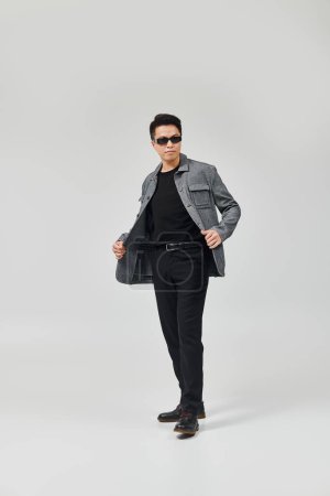 Téléchargez les photos : Un jeune homme à la mode prend une pose dynamique dans une veste grise et un pantalon noir. - en image libre de droit