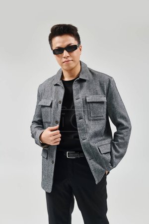 Un jeune homme à la mode pose dans une tenue élégante, portant des lunettes de soleil et une veste.