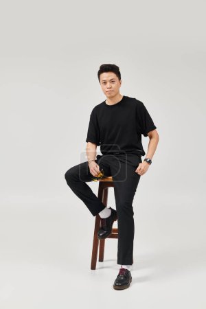 Photo for A young man in elegant attire sits on top of a wooden stool with a stylish and active pose. - Royalty Free Image